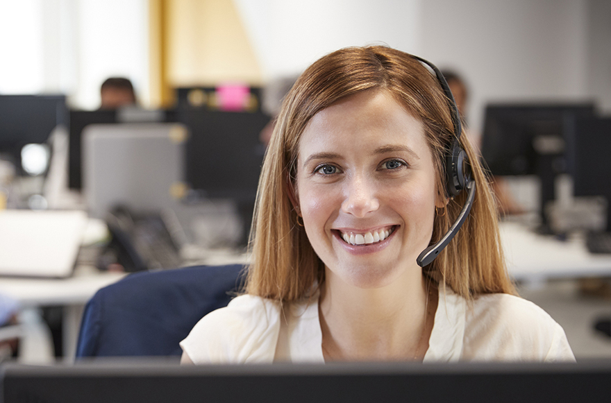 Young woman working at computer with headset in busy office